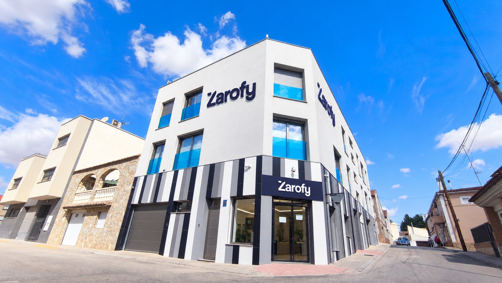 Edificio de esquina con fachada blanca, entrada acristalada y rótulos de Zarofy.